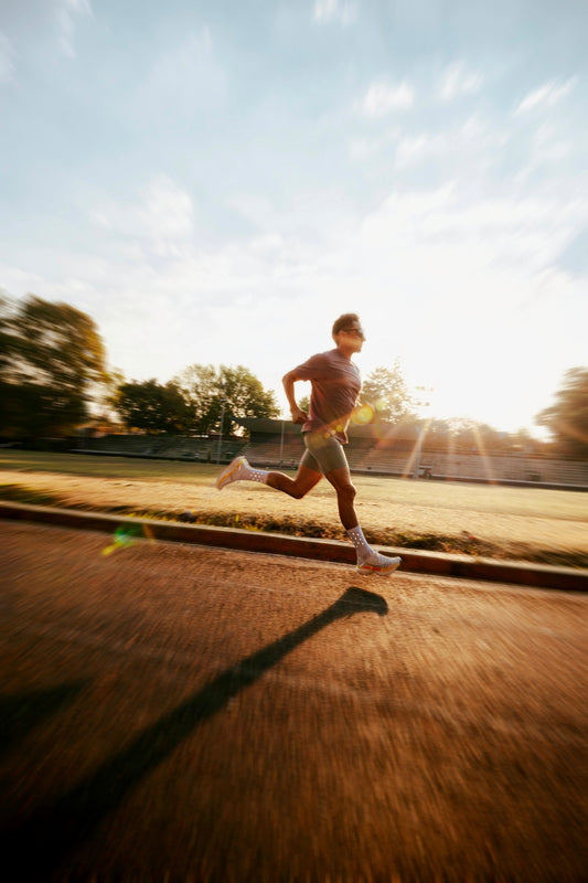 Man running on track during sunrise with lens flare.